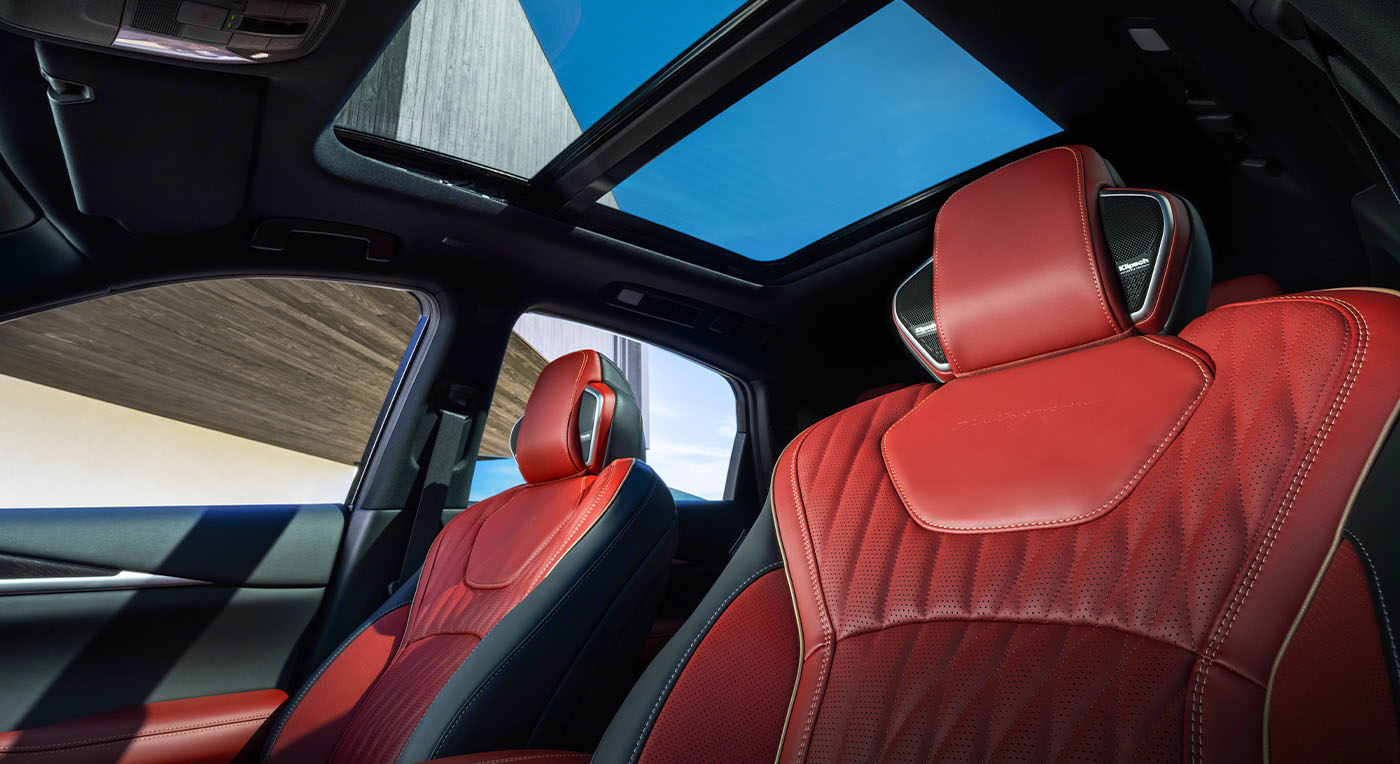 Luxurious car interior of Infiniti QX65 with vibrant red leather seats and a panoramic sunroof, set against a modern architectural background. The tone is sleek and sophisticated.